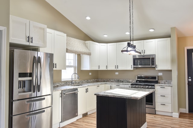 kitchen with a sink, vaulted ceiling, white cabinetry, and stainless steel appliances