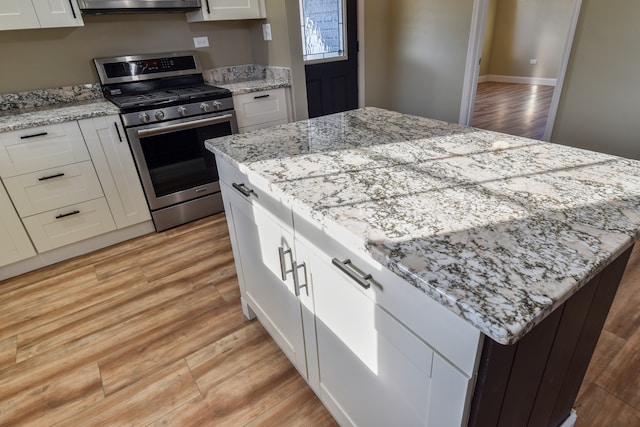 kitchen with light stone counters, light wood finished floors, white cabinets, gas range, and a center island