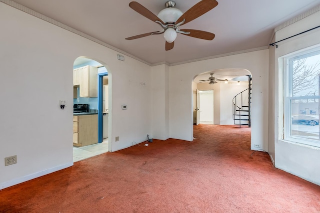 spare room with arched walkways, light carpet, a ceiling fan, ornamental molding, and stairway