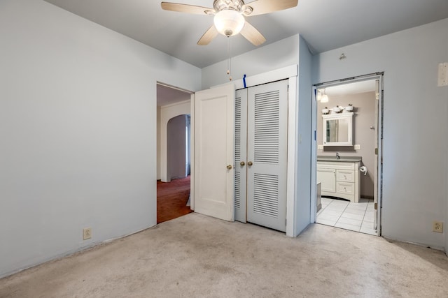 unfurnished bedroom with light carpet, a closet, arched walkways, ensuite bathroom, and a sink