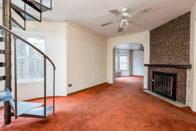 unfurnished living room featuring arched walkways, ceiling fan, ornamental molding, a brick fireplace, and carpet