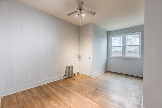 spare room featuring a ceiling fan, baseboards, light wood-style flooring, and radiator heating unit