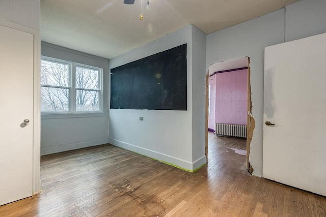 spare room featuring radiator heating unit, baseboards, and wood-type flooring