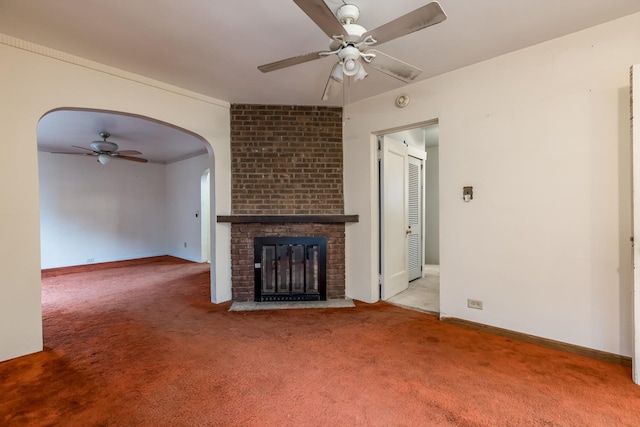 unfurnished living room with carpet floors, arched walkways, a ceiling fan, a brick fireplace, and baseboards