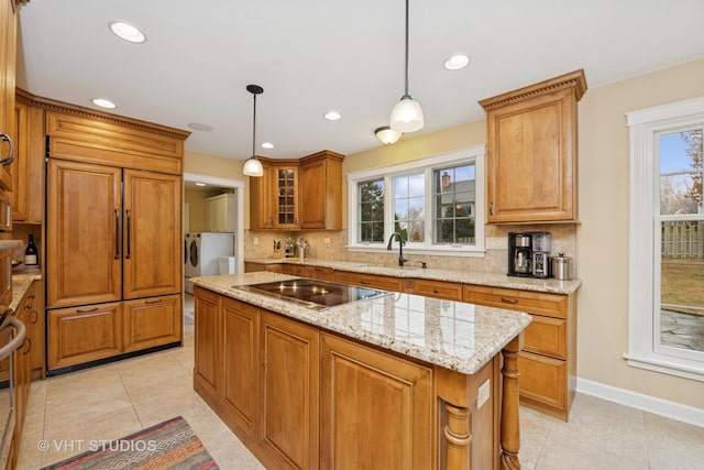 kitchen with decorative backsplash, brown cabinetry, a sink, light stone countertops, and black electric cooktop