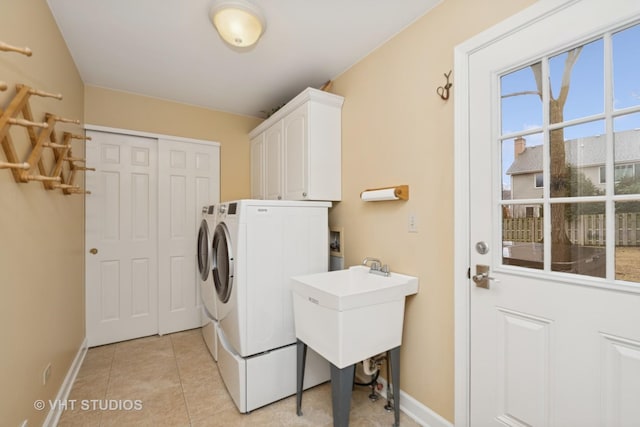 washroom featuring cabinet space, baseboards, washing machine and dryer, a sink, and light tile patterned flooring