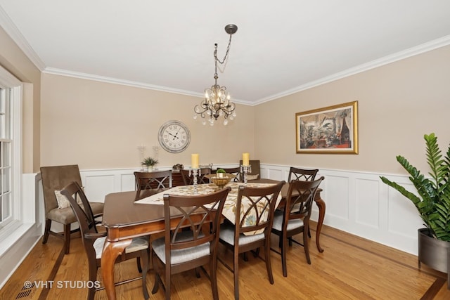 dining space with a wainscoted wall, ornamental molding, light wood-style flooring, and an inviting chandelier