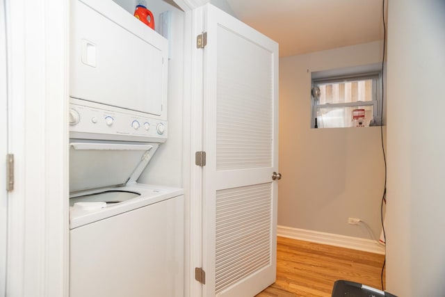 clothes washing area featuring light wood finished floors, laundry area, stacked washing maching and dryer, and baseboards