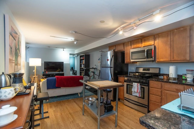 kitchen featuring brown cabinets, rail lighting, stainless steel appliances, and light wood-type flooring