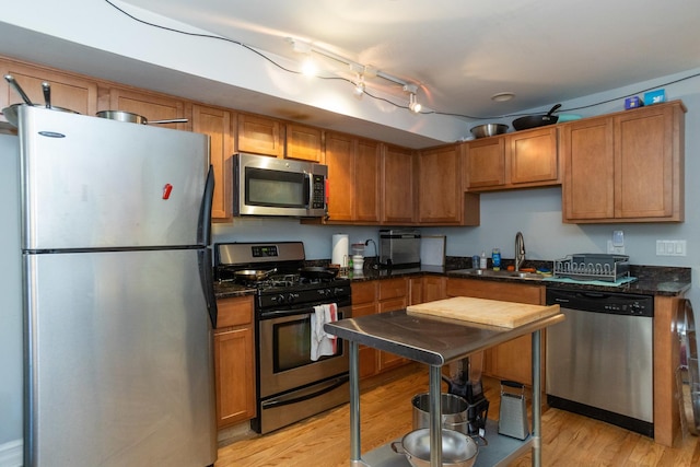 kitchen with brown cabinets, a sink, stainless steel appliances, dark stone counters, and light wood finished floors