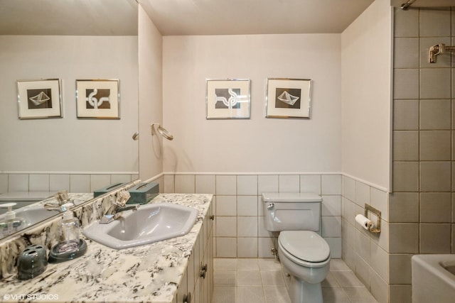 full bathroom with tile patterned floors, a wainscoted wall, toilet, a tub to relax in, and vanity