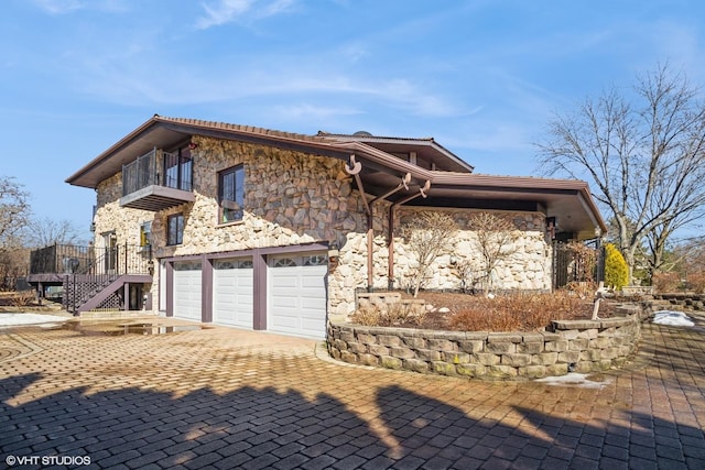 view of front of home featuring stairway, a balcony, a garage, stone siding, and decorative driveway