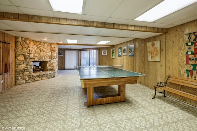 rec room with a paneled ceiling, light floors, wood walls, and a fireplace