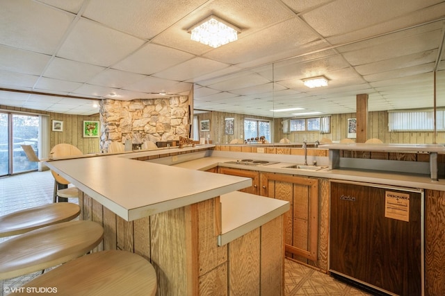 kitchen with a drop ceiling, white electric stovetop, a breakfast bar, and light countertops