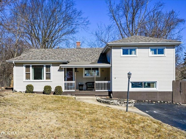 view of front facade featuring covered porch, roof with shingles, a chimney, and a front lawn