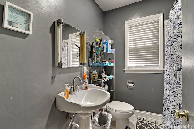 bathroom featuring tile patterned flooring, curtained shower, baseboards, toilet, and a sink