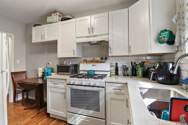 kitchen with stainless steel microwave, under cabinet range hood, light countertops, white range with gas stovetop, and decorative backsplash