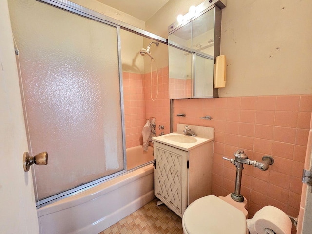 bathroom with vanity, tile walls, toilet, and bath / shower combo with glass door