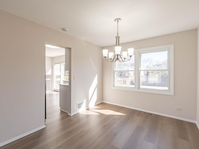 unfurnished dining area with visible vents, baseboards, a notable chandelier, and wood finished floors