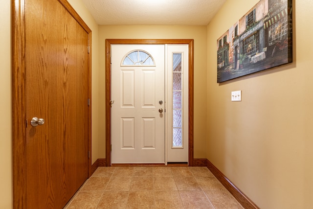 entryway with a textured ceiling, light tile patterned floors, and baseboards