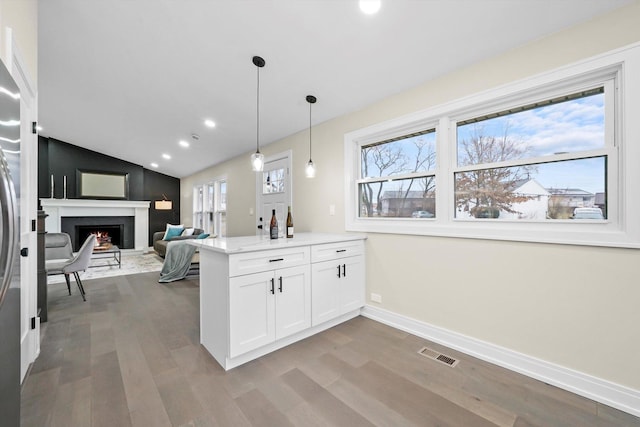 kitchen with white cabinets, a peninsula, wood finished floors, a lit fireplace, and baseboards