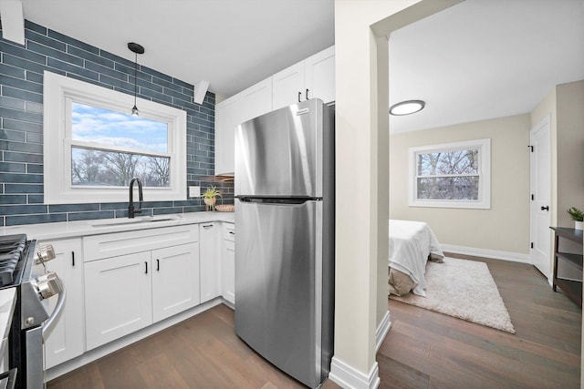 kitchen with dark wood finished floors, stainless steel appliances, decorative backsplash, white cabinets, and a sink