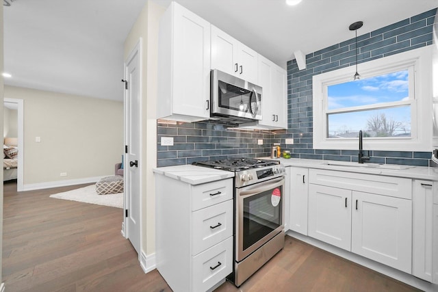 kitchen with baseboards, decorative backsplash, dark wood-style floors, appliances with stainless steel finishes, and a sink