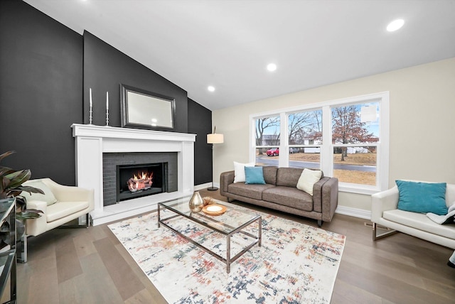 living area featuring lofted ceiling, recessed lighting, a brick fireplace, wood finished floors, and baseboards