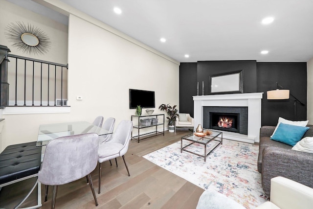 living area featuring a warm lit fireplace, wood finished floors, and recessed lighting