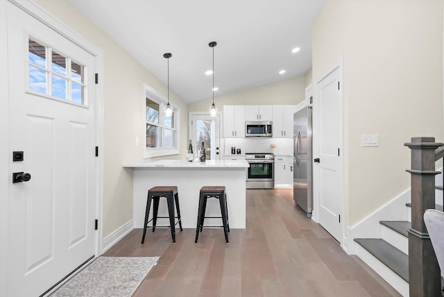 kitchen with stainless steel appliances, white cabinets, wood finished floors, a peninsula, and a kitchen breakfast bar