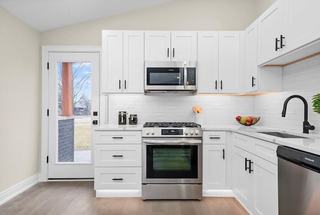 kitchen featuring lofted ceiling, appliances with stainless steel finishes, a sink, and light wood-style floors