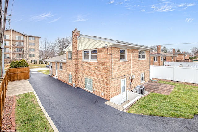 view of property exterior with brick siding, a chimney, a lawn, fence, and cooling unit