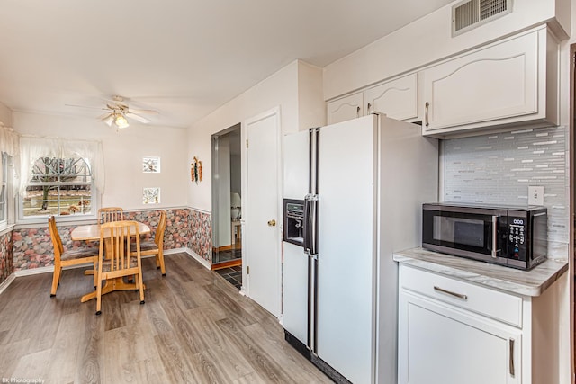 kitchen with light wood-style floors, visible vents, white fridge with ice dispenser, and stainless steel microwave