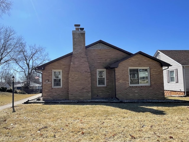 view of side of home with brick siding, a yard, and a chimney