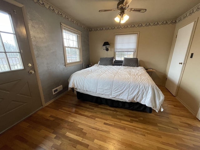 bedroom with a ceiling fan, visible vents, baseboards, and wood finished floors