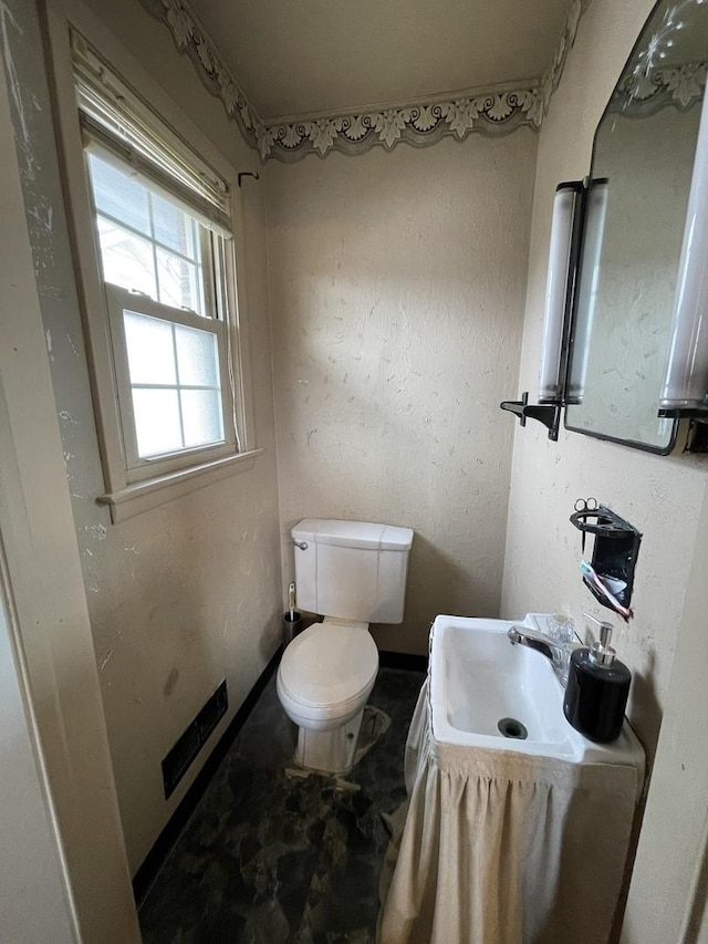 half bath featuring toilet, baseboards, and a sink