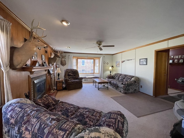 living room featuring ornamental molding, a glass covered fireplace, carpet flooring, and ceiling fan