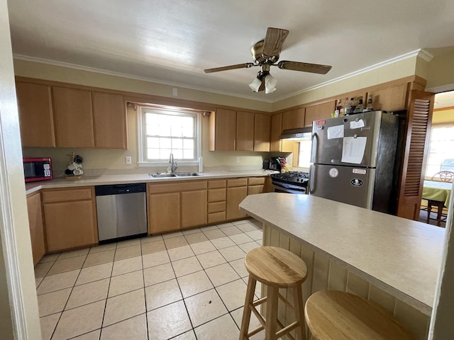 kitchen with under cabinet range hood, stainless steel appliances, a sink, light countertops, and light brown cabinetry