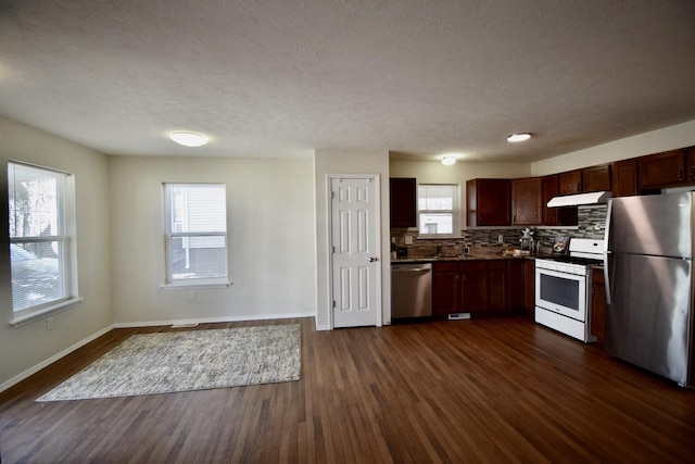 kitchen featuring backsplash, baseboards, under cabinet range hood, stainless steel appliances, and dark wood-style flooring