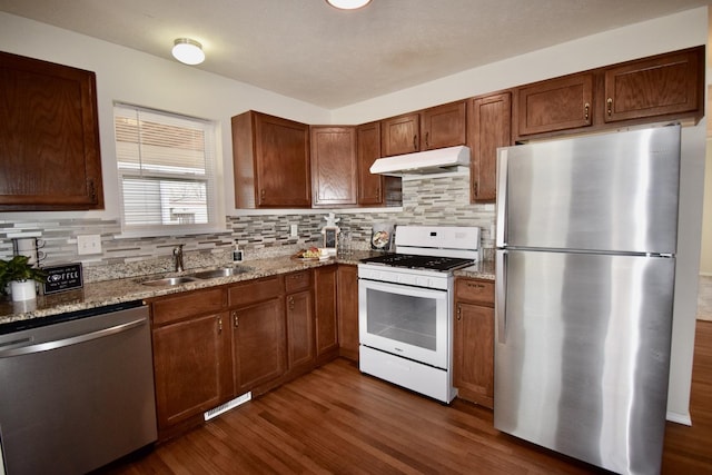 kitchen with dark wood-type flooring, light stone countertops, under cabinet range hood, appliances with stainless steel finishes, and a sink