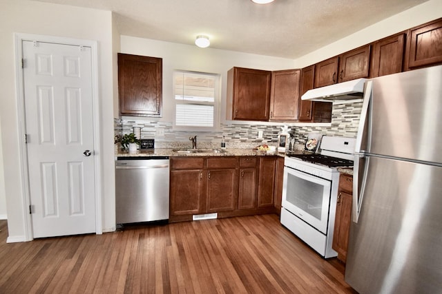 kitchen with under cabinet range hood, light stone counters, a sink, wood finished floors, and appliances with stainless steel finishes