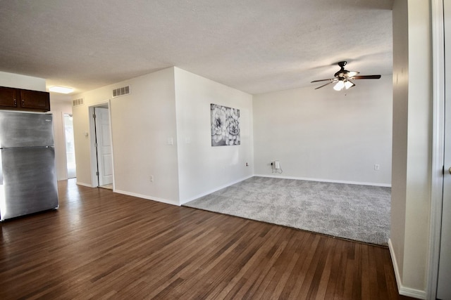 unfurnished living room featuring visible vents, a textured ceiling, dark wood finished floors, baseboards, and ceiling fan