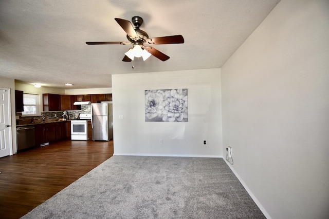 unfurnished living room with dark colored carpet, baseboards, dark wood finished floors, and ceiling fan