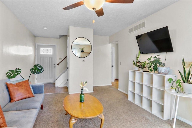 living area featuring visible vents, a textured ceiling, baseboards, ceiling fan, and stairs