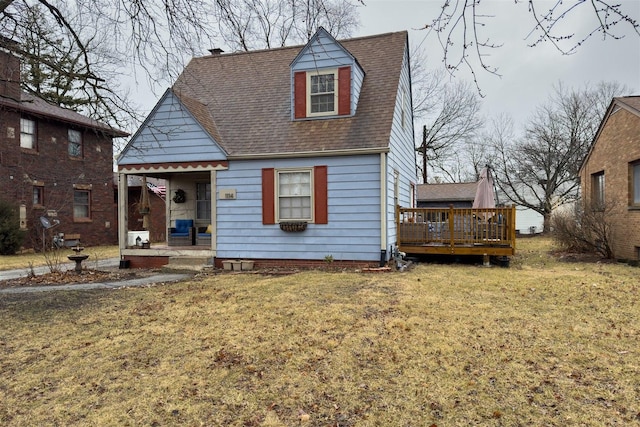 view of front of house with roof with shingles, a deck, and a front lawn