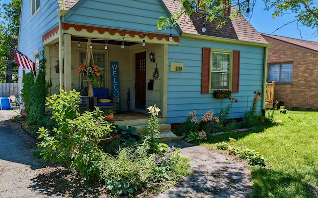 bungalow featuring a shingled roof, covered porch, and a front lawn