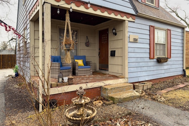 entrance to property featuring a porch, roof with shingles, and fence