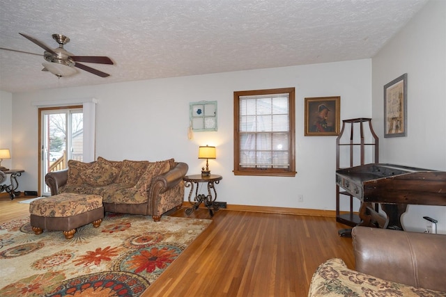 living room featuring ceiling fan, a textured ceiling, baseboards, and wood finished floors