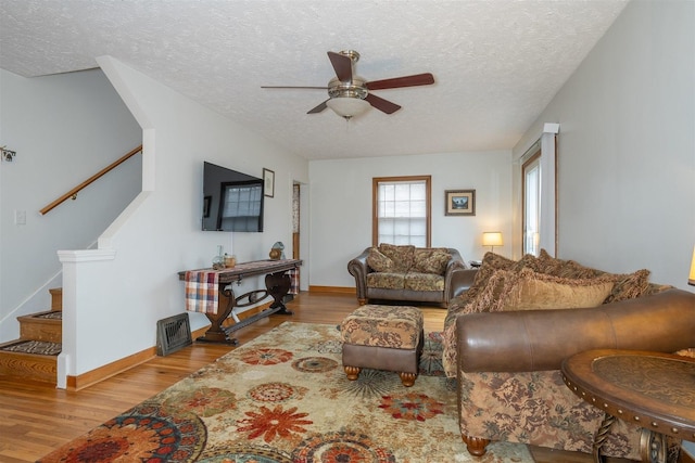 living room with a textured ceiling, wood finished floors, a ceiling fan, baseboards, and stairway