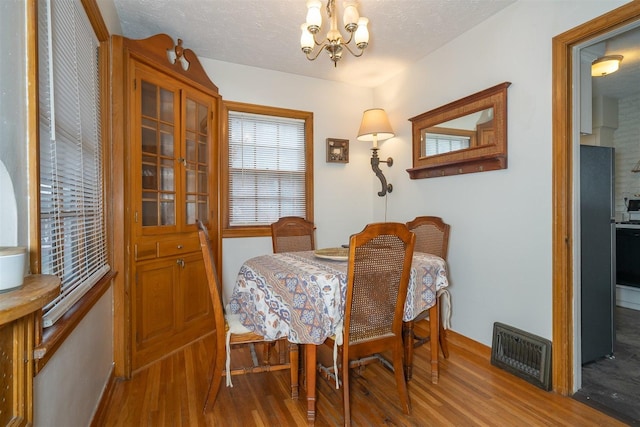 dining space with a textured ceiling, wood finished floors, visible vents, and a notable chandelier